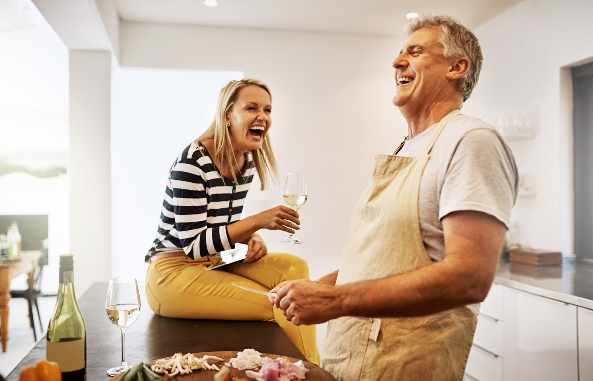 Mature couple laughing while cooking dinner and drinking wine